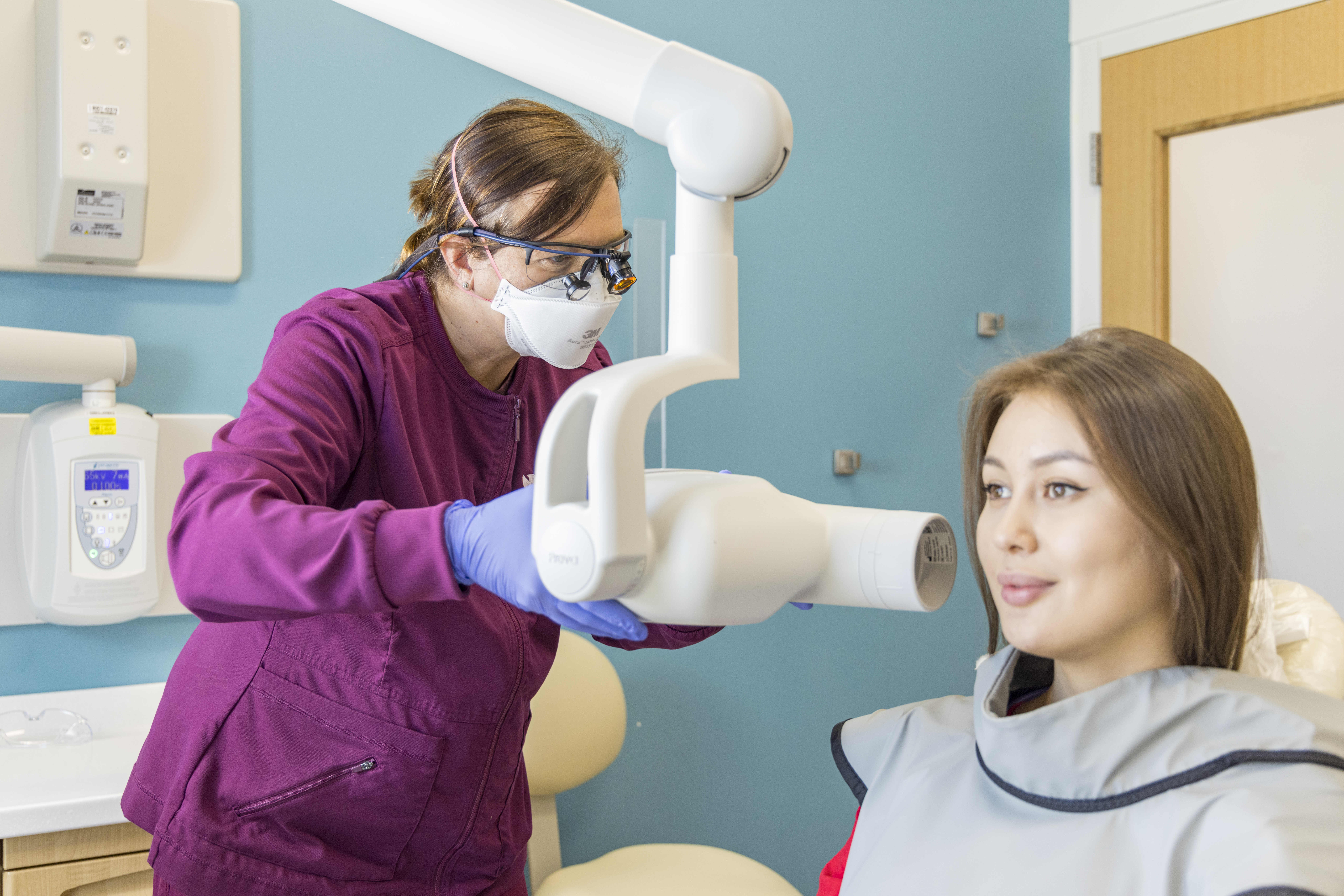 Dental hygienist in purple scrubs takes x-rays of patient's teeth