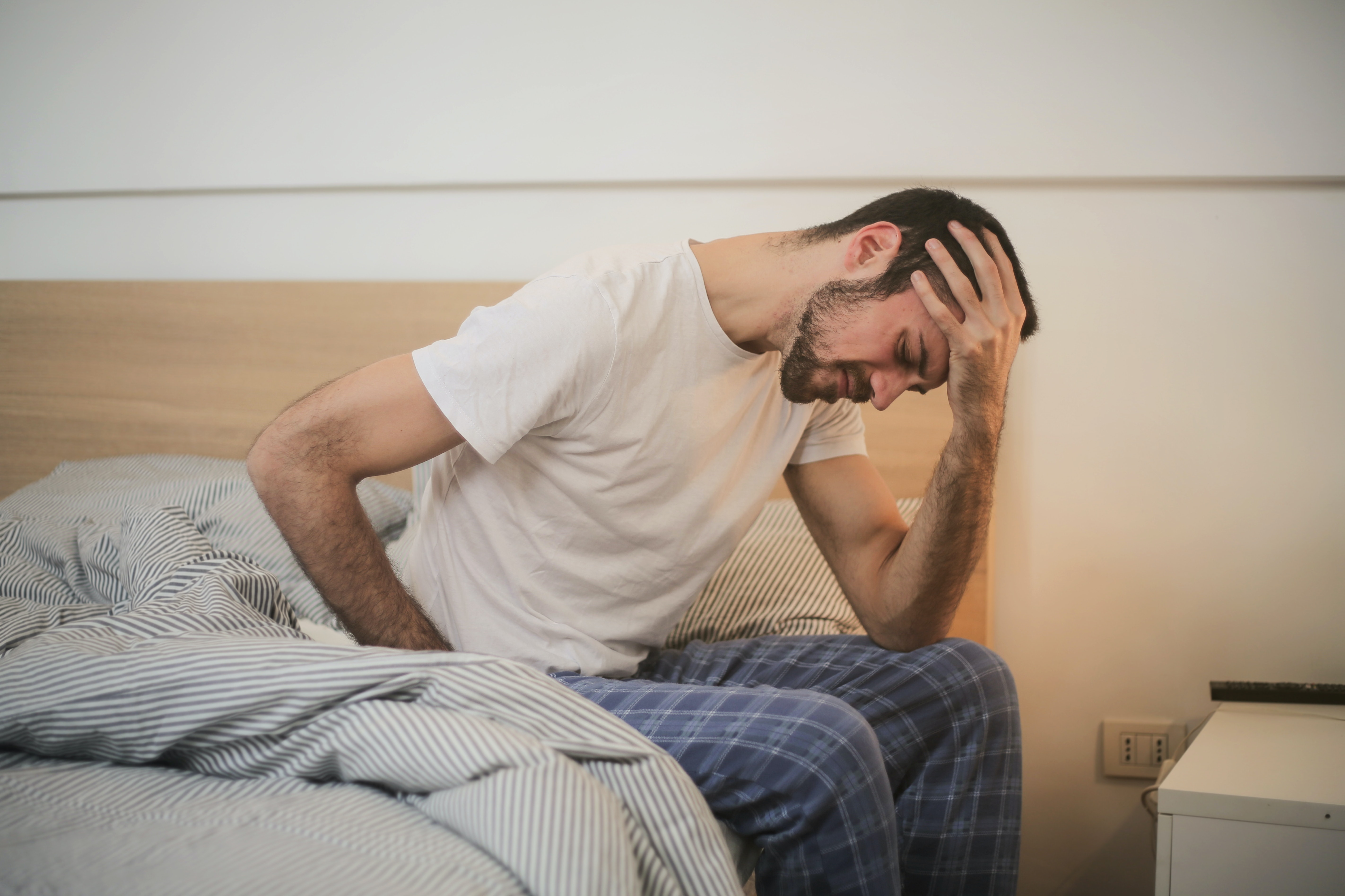 Man sitting on the edge of his bed holding his head with his hand