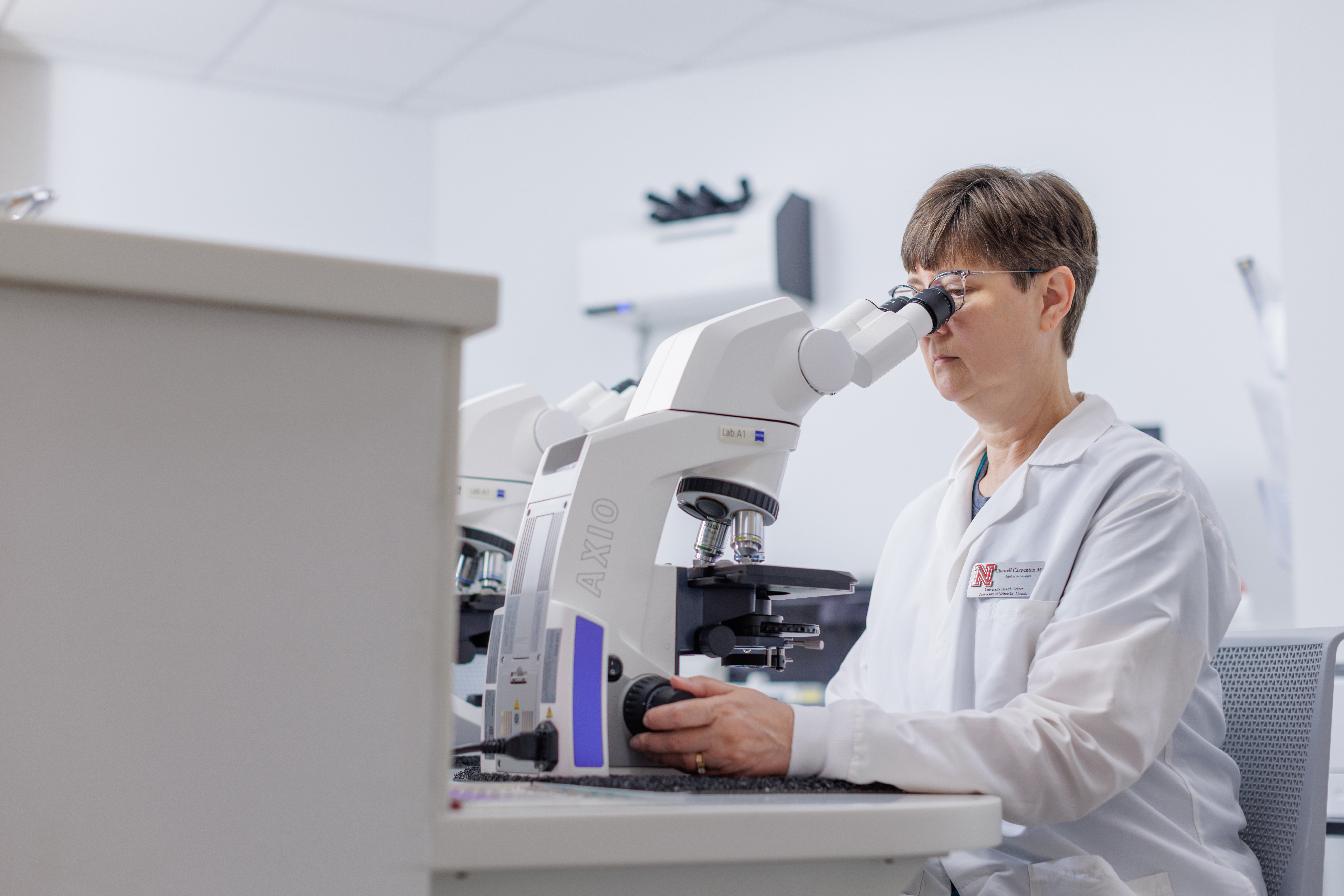 Lab employee in white coat looks into microscope