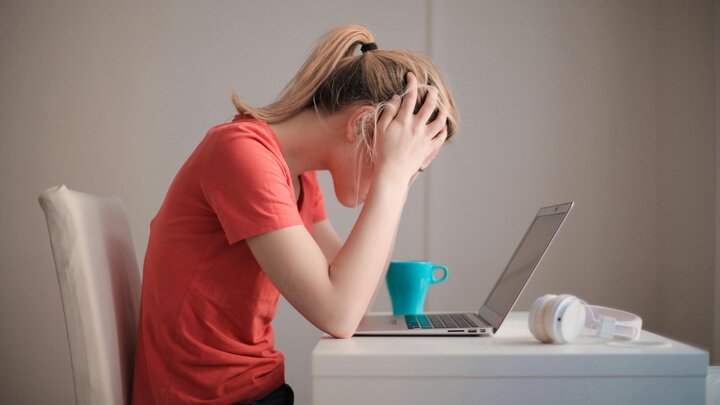 woman leaning over laptop with hands on head