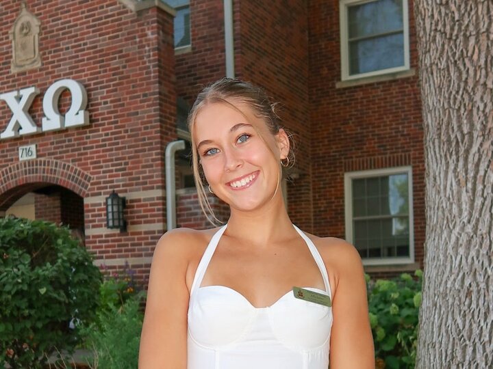 Person in white dress standing in front of brick building